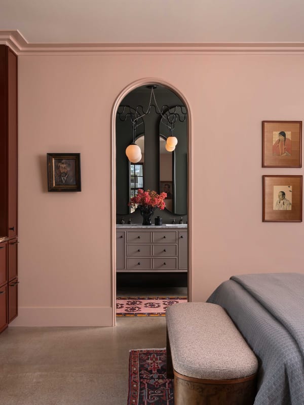 A pink bedroom seen past an arched doorway, with red built-in cabinetry alongside.