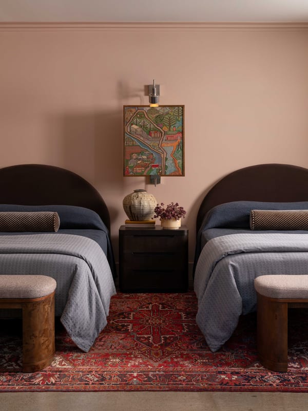 Twin beds with rounded upholstered headboards on a red patterned rug, under a pink ceiling.