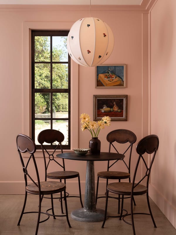 A pink breakfast nook with a pedestal table, metal bistro chairs and a paper lantern.