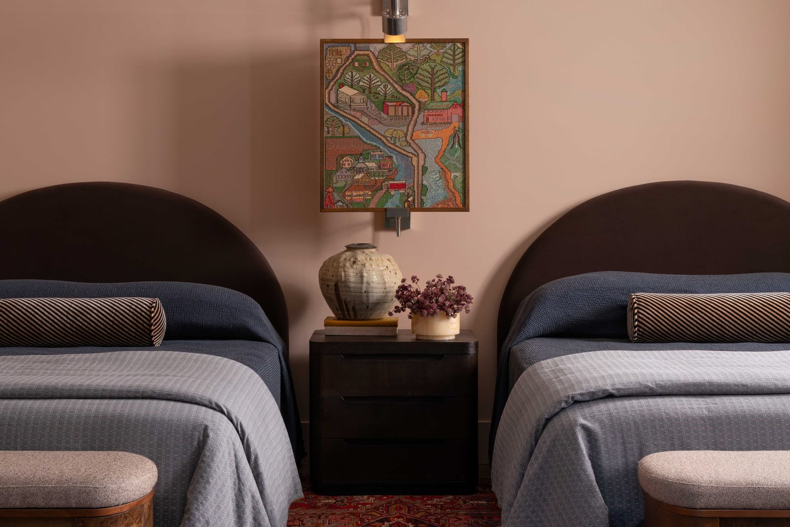 Twin beds with rounded upholstered headboards against a pink wall, a framed map between them.