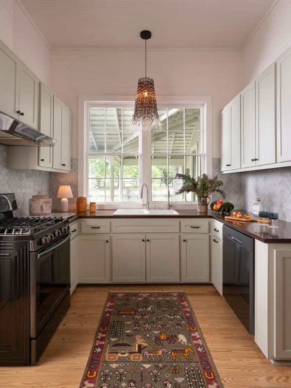 A kitchen with a black range, open shelving and a patterned runner on wood floors.
