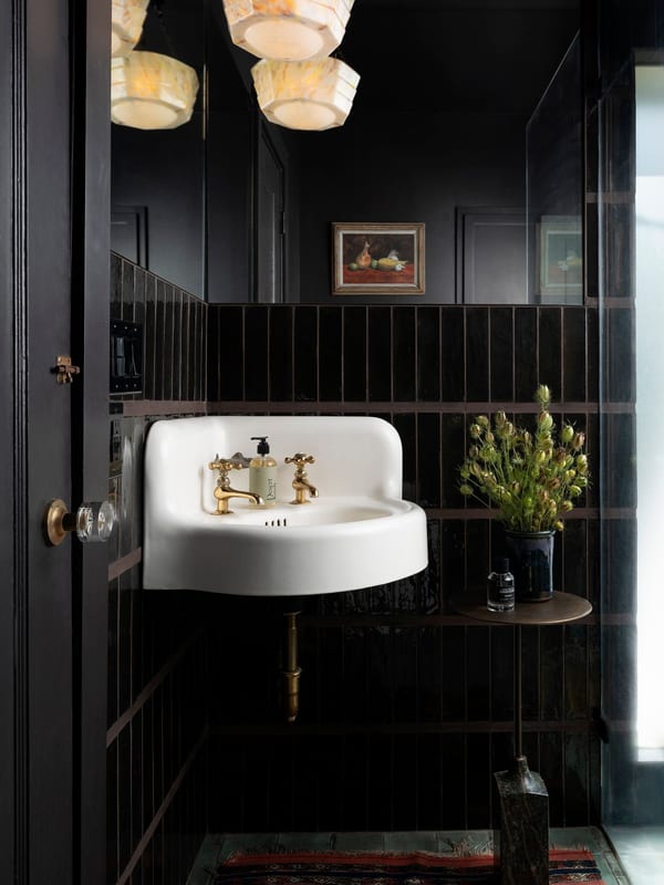 A black-panelled powder room with a wall-mounted sink and brass fittings.